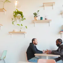 Photograph of two men seated at a two-top in a cafe. 