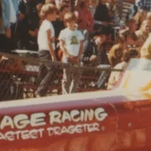 Archive photo of brown haired white woman Kitty O'Neil, race car driver, behind the wheel of red cigarette dragster car with painted words on it "space age racing worlds fastest dragster."