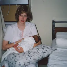 A photo of a young white woman holding a newborn baby up to her breast. She’s in a hospital room and looks slightly out of it.