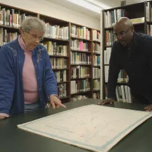 Dr. Omar Price, historian, and Susan Pearl, Librarian and Historian of Prince George's County, Maryland Historical Society are reviewing a historic 1800s map and are pointing out former Freedmen Bureau School Sites in the County. They are in the library of the Historical Society.