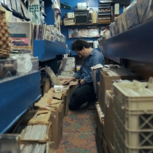A white man flips through crates of records while kneeling on the ground.