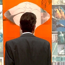 The back of a man in a suit as he stands in front of colorful artwork