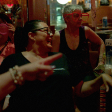 A group of middle-aged women dance in a dimly-lit bar.