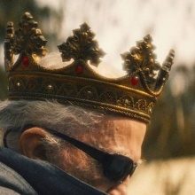 A profile view of a man wearing a crown and sunglasses.
