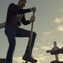 From below, a man digs a grave.