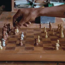 A hand hovers over a chess board.