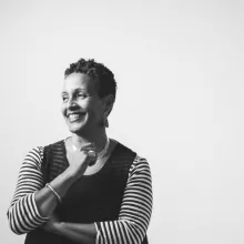 A black and white photograph of a smiling Black woman with short hair. She is wearing a dress with striped sleeves.