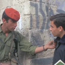 Two men face each other in front of a stone wall.