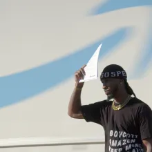 black man shades his face with a paper in front of an amazon logo