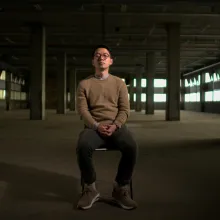 an asian man sits in the middle of an abandoned warehouse 