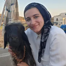 A person with a head scarf hugs and goat and smiles.