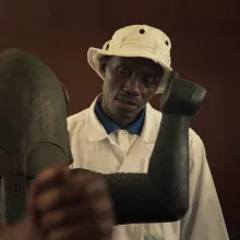 Black man in white bucket hat looks over an artifact.