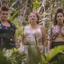 three people stand in a row in a jungle setting. they are wearing elaborate and beautiful outfits.