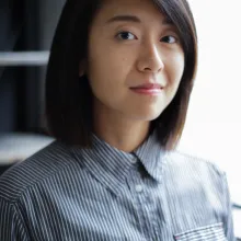 Professional headshot of asian person with a blue button up. their black hair swoops.