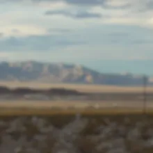 Wide landscape of a desert with a mountain in the background and a light blue sky. 