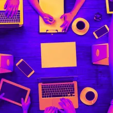 A neon-colored stock image of a table full of people working on computers and laptops.