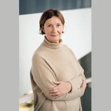 A light-skinned woman with cropped brown hair and a beige sweater gently smiles at the camera.