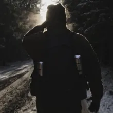 Backlit by the sun, the silhouette of a man walking down a snowy road.