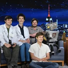 This is a group of friends sitting on a couch and floor at the tonight show. There is also a robot in the photo.