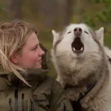 A blond young woman looks at a howling dog.