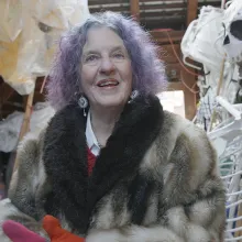 Halloween Parade director Jeanne Fleming, with purple hair and a flamboyant fur coat, stands in awe in the barn where she stores fifty years of puppets.