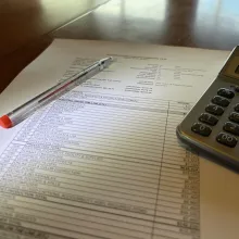 Photograph of a print out of a budget topsheet, a pen, and a calculator.