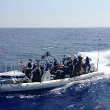 A small boat with around a dozen people motors toward shore.