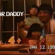 Screenshot of a VHS tape recording of a father and his two young children sitting at a table, in front of a birthday cake with a number four candle on it. The date on the tape reads Jan 12 1995.