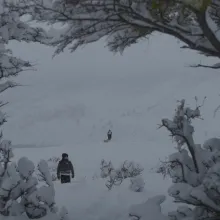 A silhouette of a solitary figure on horseback rides through a snowy Patagonian landscape in Chile.  Snow covered shrubbery in the foreground with jagged mountains in the background.  The plains in bewteween where the man on horseback is covered in fog.