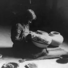 Old black & white photograph of a person sitting on the ground decorating pottery