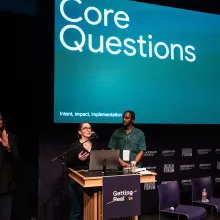 Two presenters stand at the podium, giving a talk during Getting Real '24. The slide behind them reads "Core Questions." 