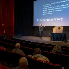 Davide Abbatescianni stands on a stage giving a talk. Behind him is a slide in blue captioned "Collaboration is key."   