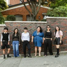 Six women stand against a brick wall.