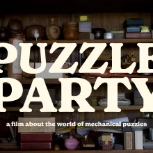 A wood cabinet with shelves full of mechanical puzzles. The puzzles are all manners of shapes and sizes, and crafted from a variety of materials. Text on the screen reads Puzzle Party, a film about the world of mechanical puzzles.