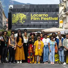 A large group of smiling people wearing Locarno merchandise pose in front of a festival banner.