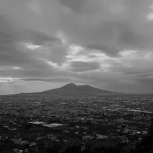 Under an overcast sky, a volcano looms over the city of Naples.