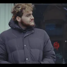 A young man wearing a puffy jacket looks to the side.