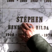 A hand tenderly touches a plaque that reads: "Stephen / Henry Hilda."