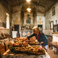 A 60-something-year-old woman examines baskets of apples on a table in a 14th Century church.