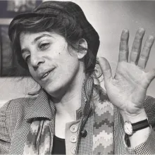 Black and white photo of a white woman with dark hair pulled back under a hat, wearing a scarf and a coat