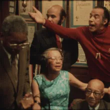 Grainy photo of a group of older Black men and women arguing in a living room