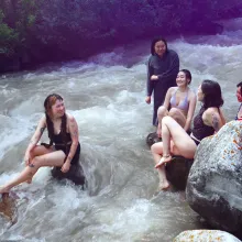 A group of soaked women gather around a riverbed, with pink smoke gathering around them
