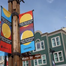 Street lamp posters advertising the 2026 Sundance Film Festival with a view of Main Street buildings against a bright blue sky