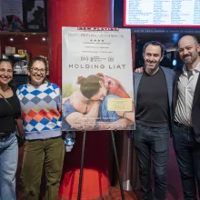 Around a poster of Holding Liat at a movie theater lobby stand two men to the right and two women on the left.
