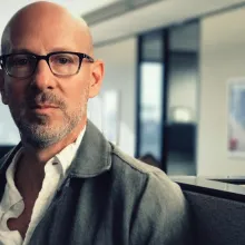 A man with white skin looks at the camera. He wears glasses, a grey jacket, white shirt and is bald and has a light beard. Headshot of Joshua Seftel