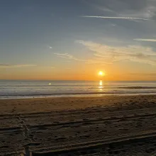 A Malibu beach at sunset with the sun over the ocean and gentle waves along the shore.