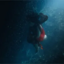 Dark shot of a woman in a red dress floating underwater, her black hair curling up