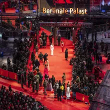 Outdoor, nighttime shot of a red carpet at the Berlinale Palast where photographers crowd folks dressed up near them