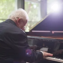 Over the shoulder shot of an older man wearing a suit jacket playing the piano