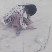 Young girl in floral top crouched over barren ground